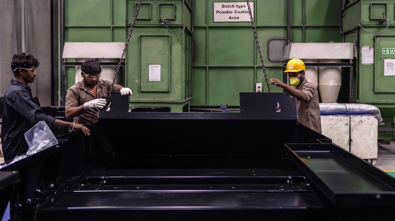 Operators loading a steel sheet onto the cutting bed beside the coating plant