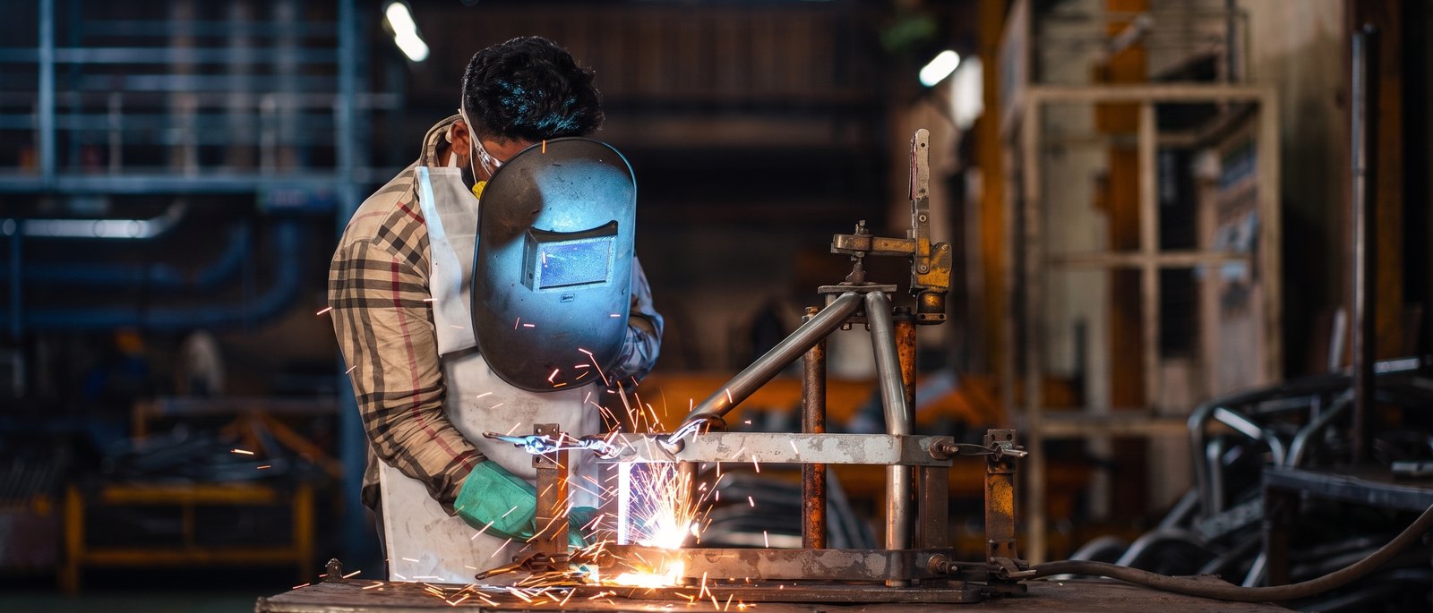 A welder running a bead at the bench, sparks falling across the fixture