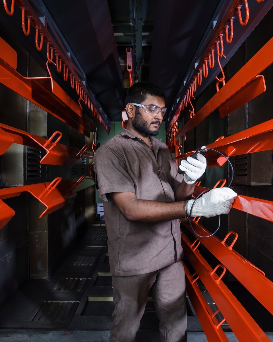 An operator in the coating booth checking a rack of finished orange components