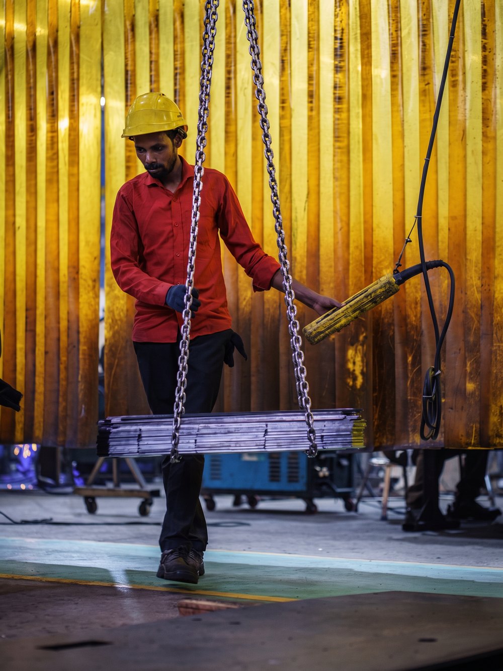 A worker guiding a crane-lifted fabricated part through the plant