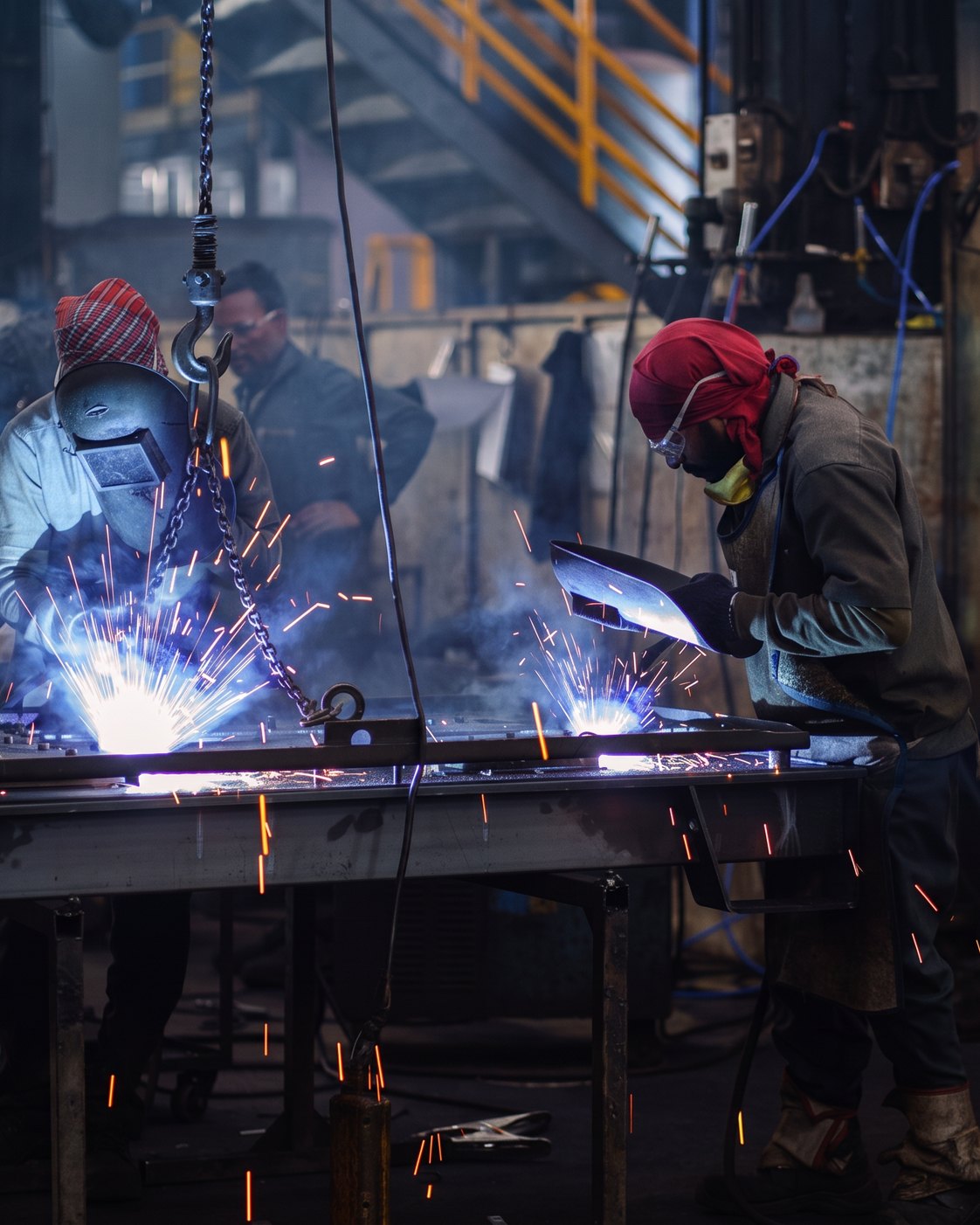 Two welders working a fabricated frame at the bench, spark fall across the table